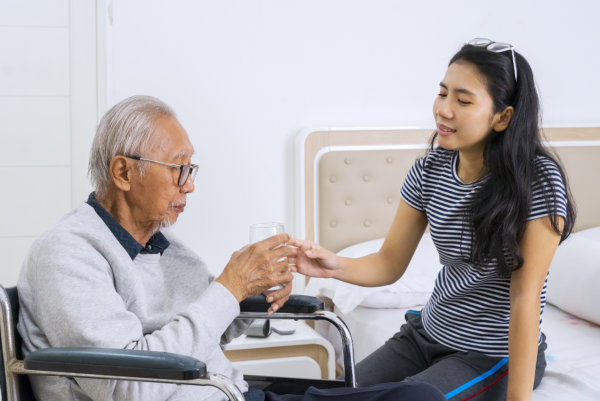 young woman giving water to elderly man